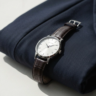 Elegant dress watch with a minimalist design on a dark leather strap, next to a folded suit jacket