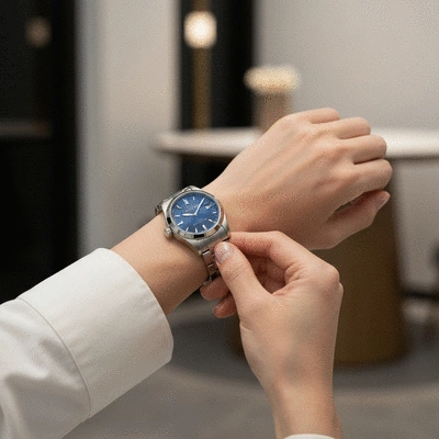 Person's hand adjusting a luxury watch on their wrist, in a well-lit, sophisticated setting