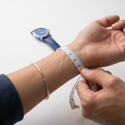 Person's wrist being measured with a soft tape measure, a watch in the background, clean image, no text, no words, no typography